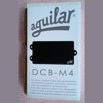 Fotografie znázorňuje černý snímač do basové kytary v originálním bílém obalu. Na obalu je nápis aguilar a modelové označení DCB-M4 spolu s popisem t…