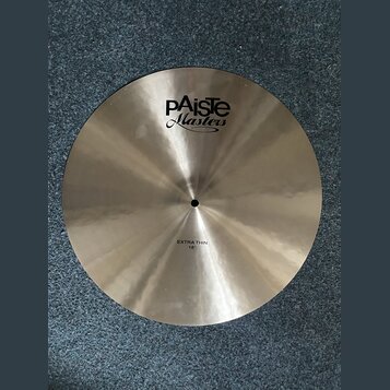 Kruhový mosazný činel s broušeným povrchem. Na povrchu je černý nápis „EXTRA THIN 18"“ a logo „Paiste Masters“. Činely vykazují mírné zaprášení.
