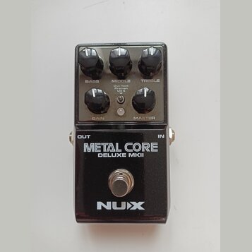 Černý kytarový efekt s nápisy METAL CORE a DELUXE MKII. V horní části jsou pět kontrolních knoflíků s popisky BASS, MIDDLE, TREBLE, GAIN a MASTER, př…
