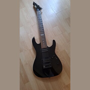 Černá elektrická kytara s tmavým hnedým hmatníkem a dvěma humbuckery. Na hmatníku je viditelný bílý štítek s nápisem "No 107". Na hlavě krku je bílé…