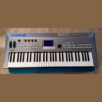 Stříbrný digitální klavír s bílými a černými klávesami. Na horní části je vlevo logo YAMAHA s doprovodným symbolem, vpravo nápis MM6 a vlevo nad kláv…