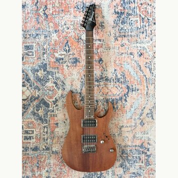 Elektrická kytara s hnědým dřevěným povrchem těla a hnedou hmatníkem. Na hlavě je bílý nápis Ibanez. Nástroj má dva humbuckery, jeden ovládací knoflí…