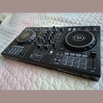 Černý DJ kontrolér s dvěma jog-koly a centrálním mixážním sekcí. Na přístroji jsou viditelný nápisy Pioneer DJ a rekordbox. Povrch je v dobrém stavu,…