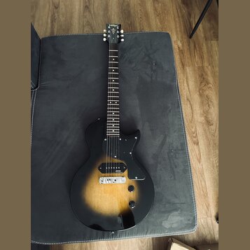Elektrická kytara s trupem v černo-žlutém sunburst provedení a černým pickguardem. Na hlavě hmatníku je viditelné logo Vintage. Nástroj má dva snímač…
