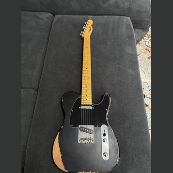 Elektrická kytara typu Telecaster s černým trupem a světle hnědým javorovým hmatníkem. Na hlavě je viditelné logo "Hagström". Trup vykazuje výrazné o…