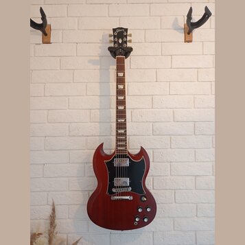 Elektrická kytara s červeným trupem v charakterickém tvaru SG a černým pickguardem. Na hlavě hmatníku je bílý nápis Gibson. Nástroj má dva humbuckery…
