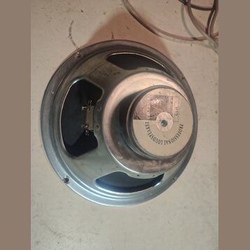 Fotografie znázorňuje zadní stranu reproduktoru s kovovým rámem a magnetem. Na bílém štítku magnetu je nápis PROFESSIONAL LOUDSPEAKER a označení G12.…