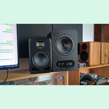 Na fotce jsou tři studiové monitory. Nejlevý vlevo je černý s nápisem ADAM AUDIO, prostřední je větší černý reproduktor s nápisy GOLD A a TAMPET v do…