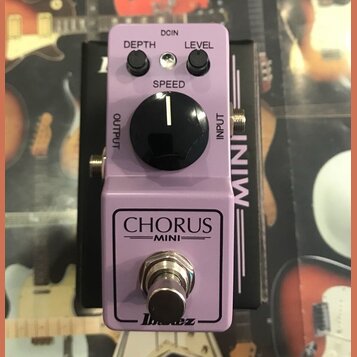 Fialový efekt pedál s nápisy CHORUS MINI a logem Ibanez. Na horní části jsou dva malé černé oválné knoflíky s popisky DEPTH a LEVEL, jeden velký čern…