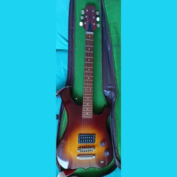 Elektrická kytara s trupem v barevnosti sunburst a hnedým krčkem, umístěná v otevřeném kufru s zeleným vnitřkem. Nástroj má jeden humbucker snímač, t…