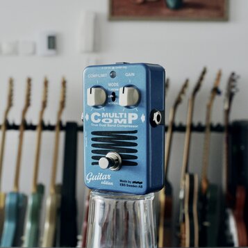 Modrý efekt pedál s kovovým povrchem. Na přední straně jsou nápisy MULTICOMP, True Dual Band Compressor, Guitar edition a Made by EBS Sweden AB. Pedá…