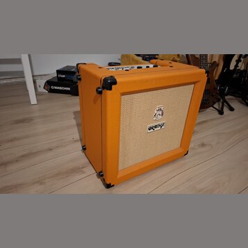 Kytarový kombozesilovač v oranžové barvě s texturovaným povrchem a béžovou přední síťovkou. Na mluvčí je umístěno logo ORANGE a nad ním malý barevný…