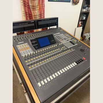 Šedý mixovací pult s nápisem YAMAHA a označením O2R. Obsahuje digitální displej, řadu posuvníků a zahlreiche ovládací tlačítka v bílé a žluté barvě.…