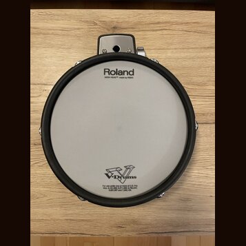 Elektronický buben bílé barvy s černým gumovým okrajem. Na membráně je nápis Roland, pod ním text MESH HEAD™ made by REMO a ve spodní části logo V-Dr…