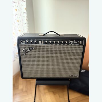 Černý kytarový kombozesilovač s šedou textilní maskou. Na horním ovládacím panelu jsou nápisy NORMAL, VIBRATO a Deluxe Reverb Amp, dále označení VOLU…