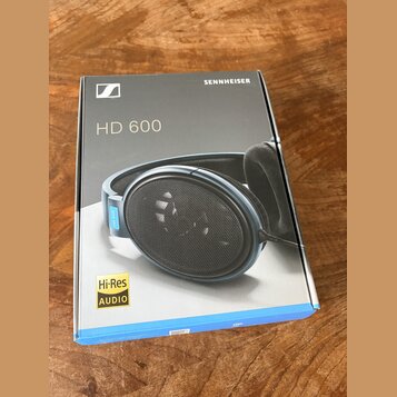Fotografie znázorňuje krabici od sluchátek. Na šedém povrchu krabice je bílé logo Sennheiser, nápis SENNHEISER a modelové označení HD 600. V levém do…