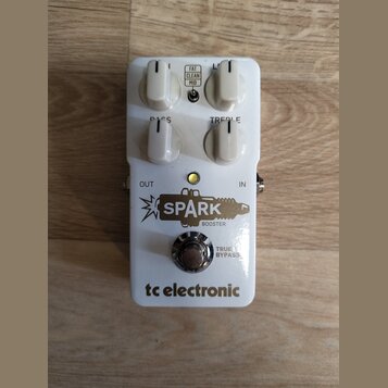Bílý efekt pedál s nápisy SPARK BOOSTER a tc electronic. Na horní straně jsou čtyři bílé otočné ovladače s popisky BASS a TREBLE, doprovázené přepína…