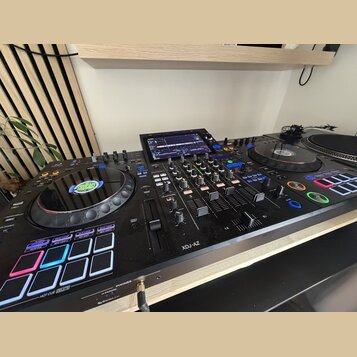 Černý DJ 컨트롤러 s integrovaným displejem a dvěma jog-koly. Na levém jog-kole je viditelné logo GRUCAST a na spodní části přístroje nápis XDJ-AZ. Zaříze…