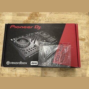 Kartonová krabice s obrázkem DJ kontroléru v černém a červeném provedení. Na krabici jsou nápisy Pioneer DJ, rekordbox a djay. Před krabicí leží průh…