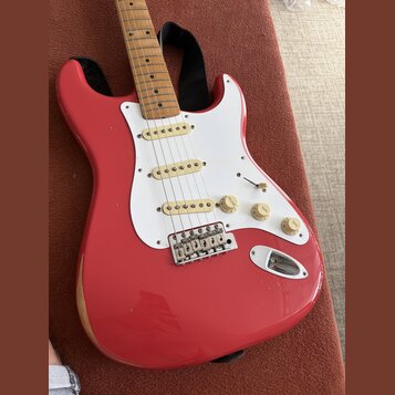 Červená elektrická kytara typu Stratocaster s bílým pickguardem a javorovým hmatníkem. Nástroj má tři bílé snímače, jeden přepínač a tři otočné poten…