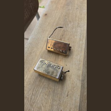 Dvě elektrické kytarové snímače typu humbucker v pozlaceném provedení. Snímač v horní části má hladký kryt s viditelnými šrouby, spodní snímač má kry…