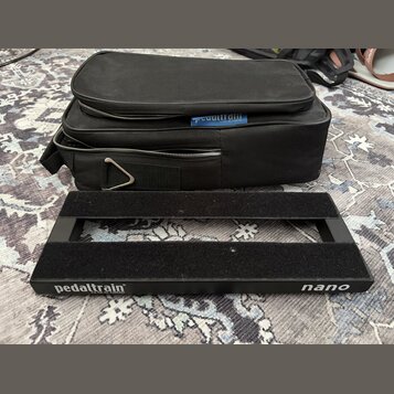 Černý kovový pedalboard s dvěma vodorovnými nosnými lištami. Na spodní hraně je bílý nápis pedaltrain® U.S. Pat. No. 7,439,023 a označení nano. Vedle…