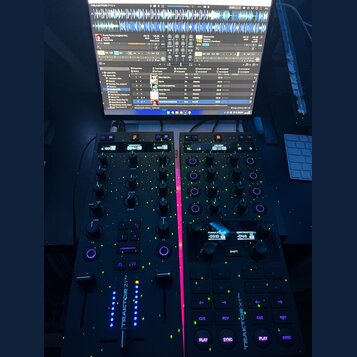 Fotografie zachycuje černý DJ kontrolér Traktor Z1, který je připojen k notebooku s otevřeným softwarem TRAKTOR PRO 4. Na zařízení jsou vidět dva mod…