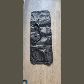 Černý obdélníkový obal z syntetického materiálu s jemným leskem. V horní části jsou dvě černé popruhy s plastovými přezkami a šitými úchyty. Povrch m…
