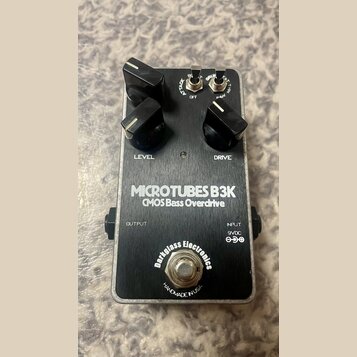 Stompbox s kovovým stříbrným povrchem a černým spodním panelem. Na horní části jsou tři černé ovládací knoflíky s popisky LEVEL a DRIVE, dva přepínač…