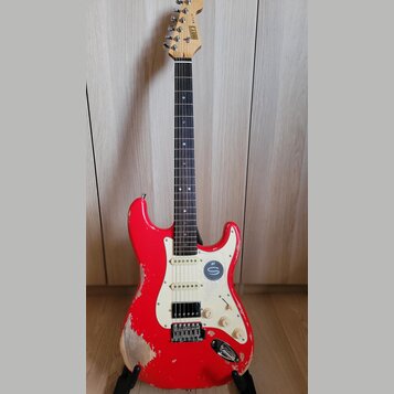 Červená elektrická kytara typu Stratocaster s bílým pickguardem a hnědým hmatníkem. Na hlavě je vidět nápis "Squier". Tělo nástroje vykazuje výrazné…