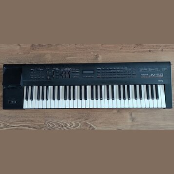 Černý digitální klávesový nástroj s bílými a černými klávesami. Na pravé straně ovládacího panelu je bílý nápis Roland JV-50 EXPANDABLE SYNTHESIZER.…