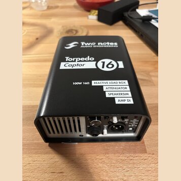 Černý obdélníkový box s kovovým povrchem. Na horní straně jsou bílé nápisy „Two notes AUDIO ENGINEERING“, „Torpedo Captor 16“ a seznam funkcí: „REACT…