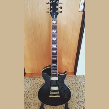 Černá elektrická kytara s tvarem singlecut a zlatým hardwarem. Na hlavě je bílé logo Ltd a svislý nápis EK-250. Nástroj má dva humbuckery s krémovými…