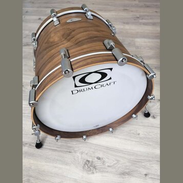 Kytlicový basový buben s dřevěným korpusem v hnědé barvě a bílým exponovaným koženem. Na koženě je černý nápis DRUM CRAFT a nad ním grafické logo. Bu…