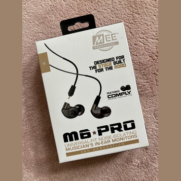 Fotografie znázorňuje krabici s in-ear monitory. Na obalu je nápis Mee PROFESSIONAL, text DESIGNED FOR THE STAGE BUILT FOR THE ROAD a FEATURES COMPLY…