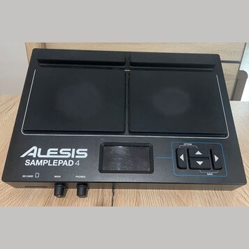 Černý elektronický samplepad s dvěma velkými gumovými pady. Na přístroji je bílý nápis ALESIS SAMPLEPAD 4 a v pravé části ovládací prvky s popisky OP…