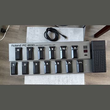 Stříbrný MIDI pedál s černými spínači a expresním pedálem vpravo. Na horní části je nápis Roland FC-200 MIDI FOOT CONTROLLER a na expresním pedálu lo…