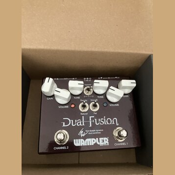 Tmavě hnědý kytarový pedál s bílými popisky a ovládacími knoflíky. Na povrchu je uveden název Dual Fusion, nápis Tom Quayle signature dual overdrives…