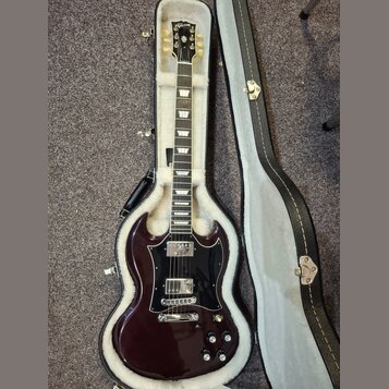 Tmavě vínová elektrická kytara s černým pickguardem v tvrdém kufru s bílou výplní. Na hlavě hmatníku je zlatý nápis Gibson. Kytara má dva humbuckery,…