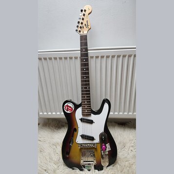 Elektrická kytara s trupem v sunburst provedení a bílým pickguardem. Na hlavě hmatníku je nápis Squier STRAT a logo Fender. Trup vykazuje výrazné opo…