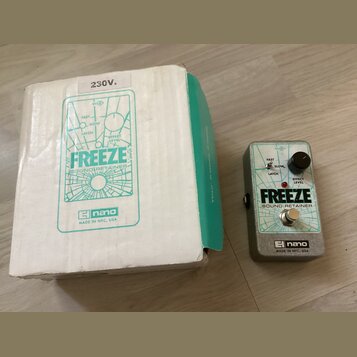 Na fotografii je efekt pedál v šedém kovovém provedení a jeho původní bílo-zelená krabice. Na pedálu i na krabici je uveden nápis FREEZE SOUND RETAIN…