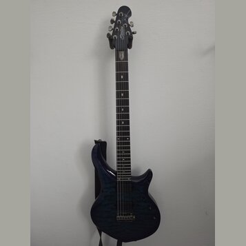 Elektrická kytara s tmavě modrým trupem s výraznou strukturou dřeva a černým hmatníkem. Na hlavě je bílý nápis Sterling by Music Man. Nástroj má dva…