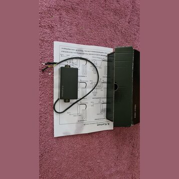 Černý plastový box s elektronikou a připojenými vodiči, položený na papírovém návodu k zapojení. Na boku boxu je bílý nápis R.M.pickups. Vedle zaříze…