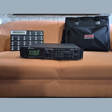Na fotografii jsou tři předměty: černý rackový procesor, černý MIDI kontrolér a černá přepravní taška. Procesor nese nápisy FRACTAL AUDIO SYSTEMS, Ax…