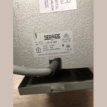 Detail štítku na šedém kovovém zařízení s texturou. Na bílém štítku je logo TRAMAG a nápisy: pri. 220 V, sec. 110 V, L.Nr. D 1601, 50÷60 Hz, 1600 VA,…