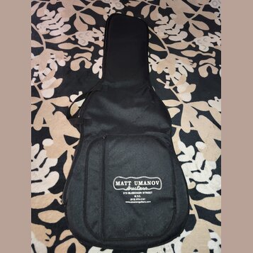 Černý polstrovaný obal na kytaru s přední kapsou. Na spodní části je bílý nápis MATT UMANOV Guitars, pod ním text 273 BLEECKER STREET N.Y.C. (212) 67…