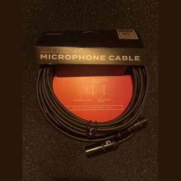 Černý mikrofonní kabel s konektory XLR, umístěný před svým originálním černým a červeným obalem. Na krabici jsou nápisy D'Addario, AMERICAN STAGE MIC…