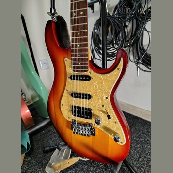 Elektrická kytara s trupem v červeno-žlutém sunburst provedení a hnědým hmatníkem. Nástroj má tři snímače (dvě jednosnívkové a jeden humbucker u koby…