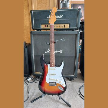 Elektrická kytara s tvarem Stratocaster, v barevné gradaci od žluté přes oranžovou po černou. Na hlavě hmatníku je viditelné logo Fender. Kytara má b…