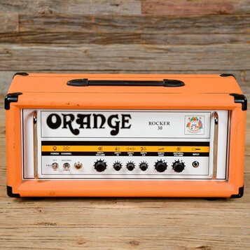 Kytarový kombozesilovač v oranžovém vinylu s černými rohy a úchytem. Na předním panelu je velký nápis ORANGE a označení modelu ROCKER 30. Ovládací pa…